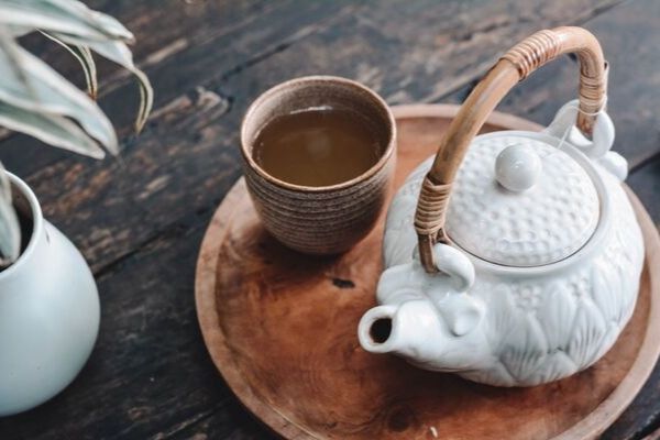 a white Japanese tea pot on a wooden tray with a tea cup on the side