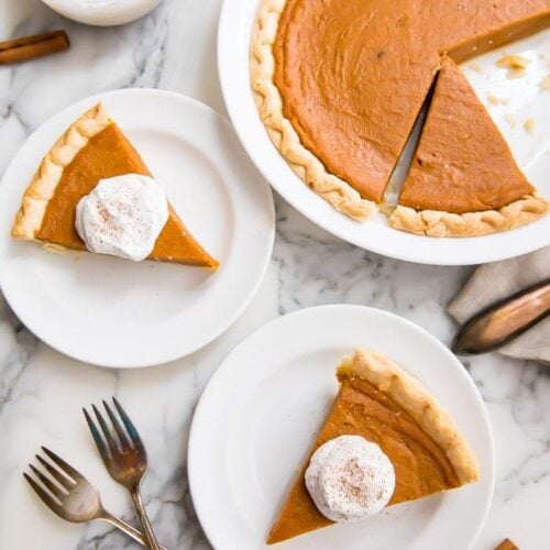 Slices of vegan pumpkin pie served with cream on white plates