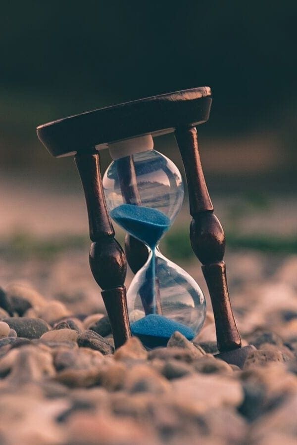 an hourglass filled with blue sand standing on pebbles 