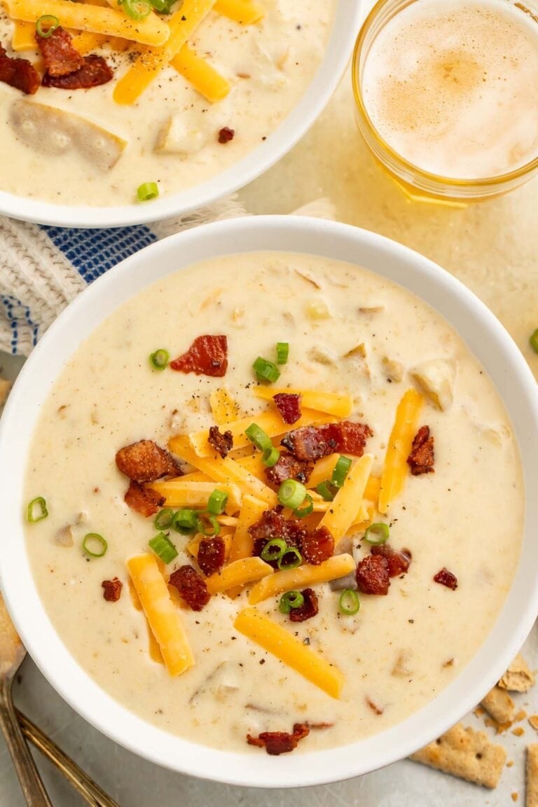 A large white bowl of creamy Crockpot potato soup topped with pieces of bacon and large shreds of cheddar cheese.