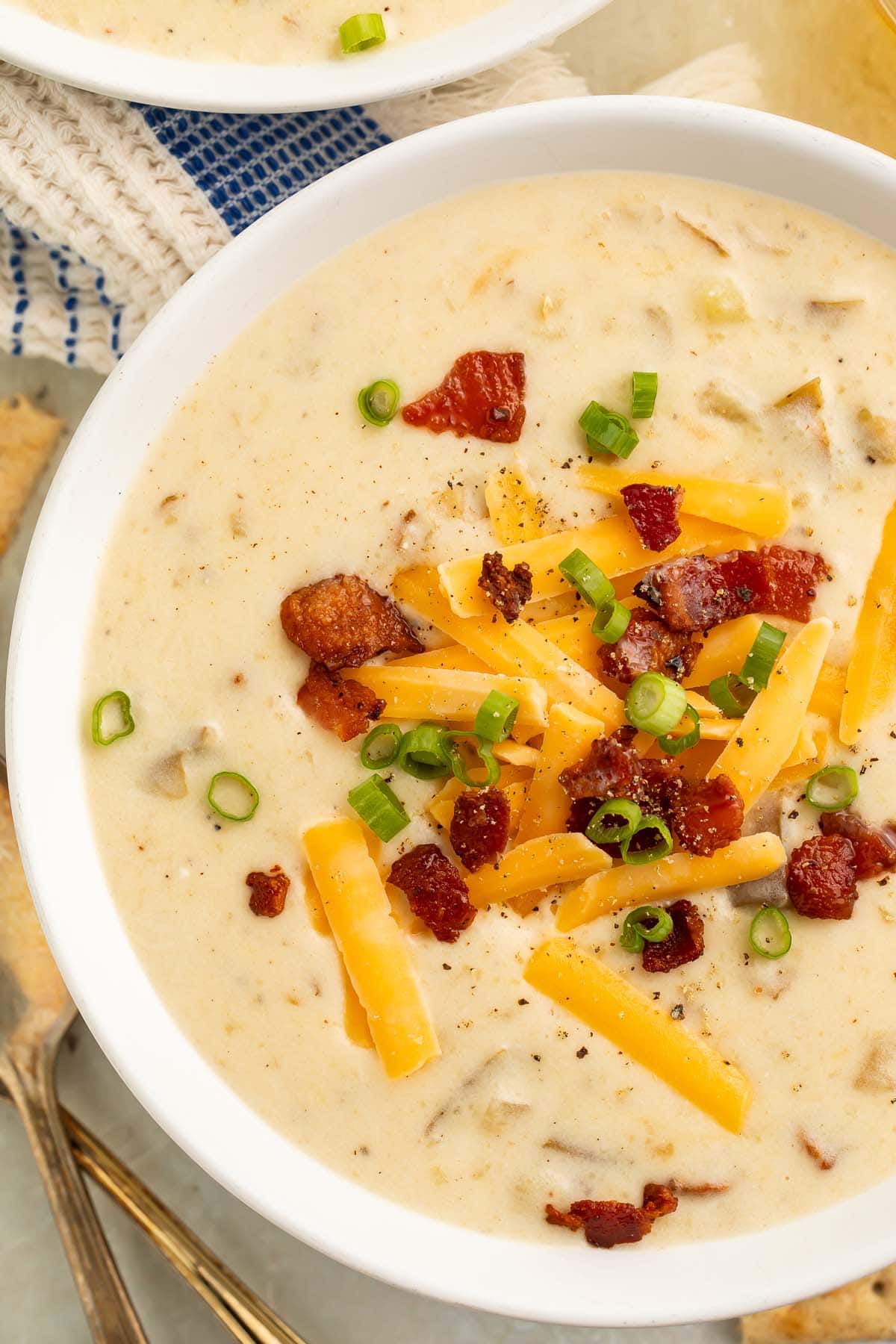 A large white bowl of creamy Crockpot potato soup topped with pieces of bacon and large shreds of cheddar cheese.