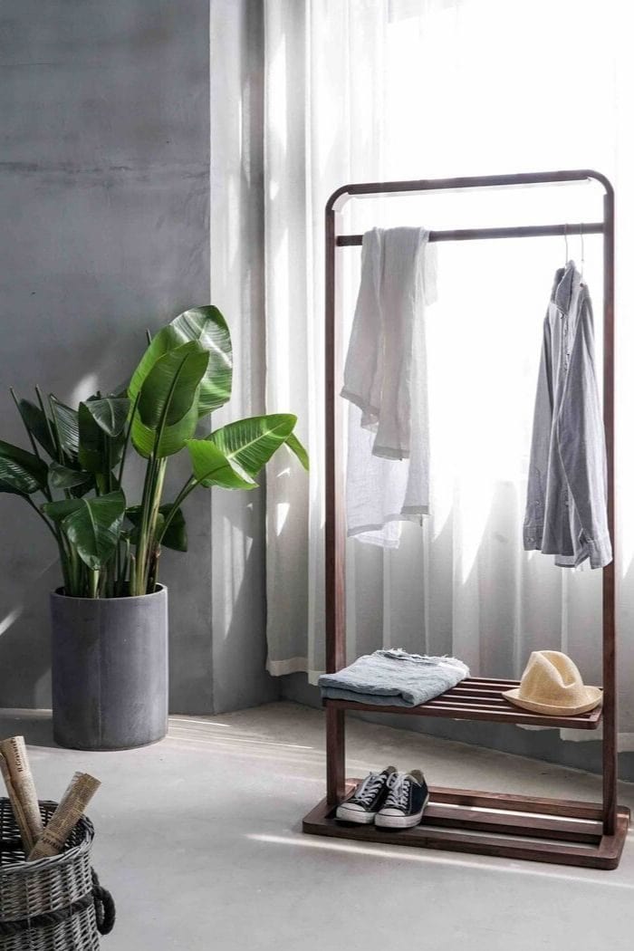 a minimalistic wardrobe with just the most basic items with a big plant next to the clothes rack