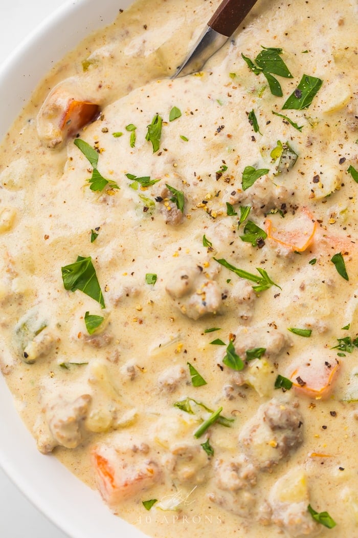 The cheeseburger soup in a white bowl garnished with fresh herbs