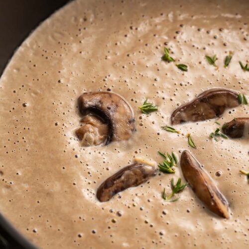 Overhead view of rich, thick, greyish-brown cream of mushroom soup in a large round black pot.