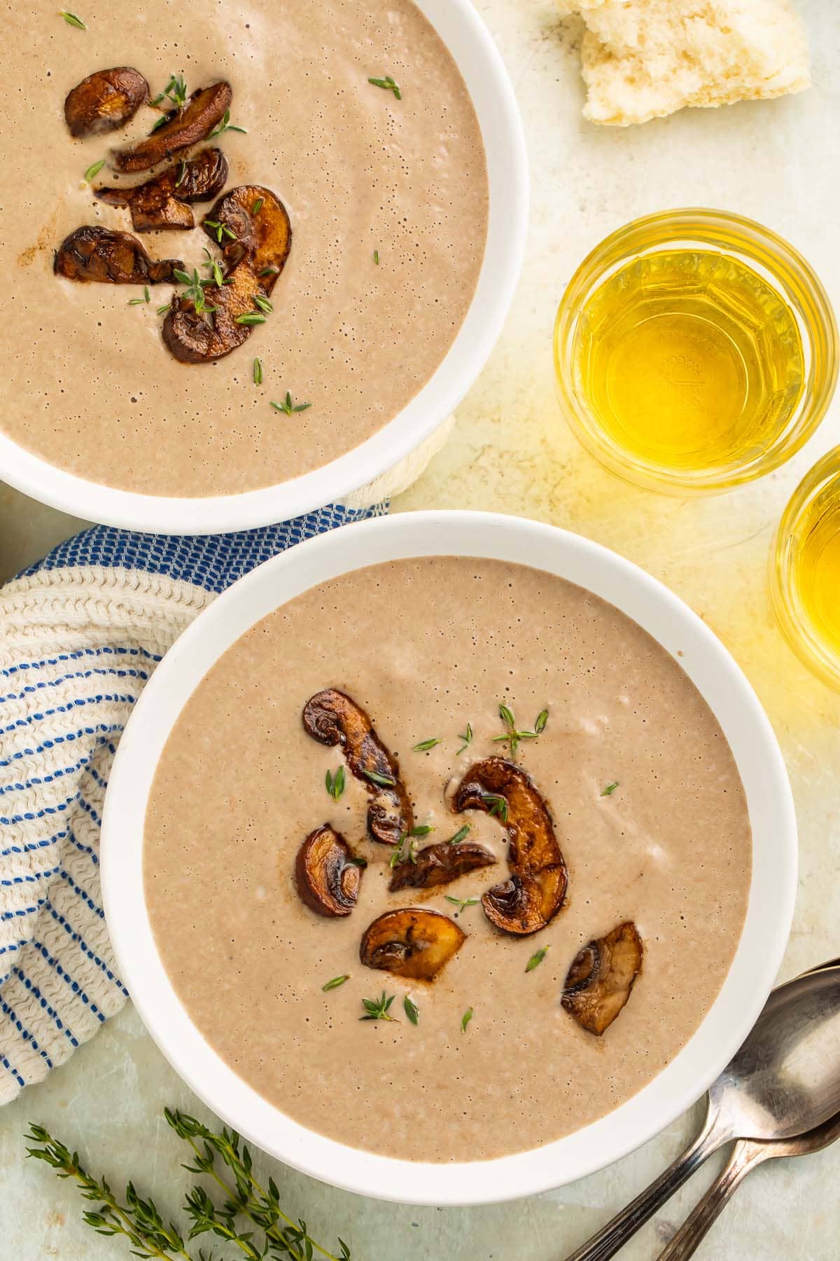 Overhead shot of 2 white bowls of greyish-brown cream of mushroom soup on a table with a napkin and a glass of wine.