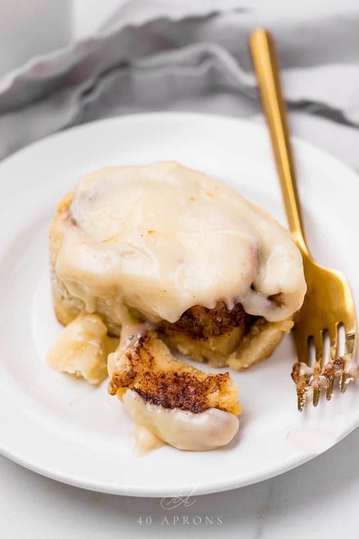 A gluten free cinnamon roll served on a white plate with a fork