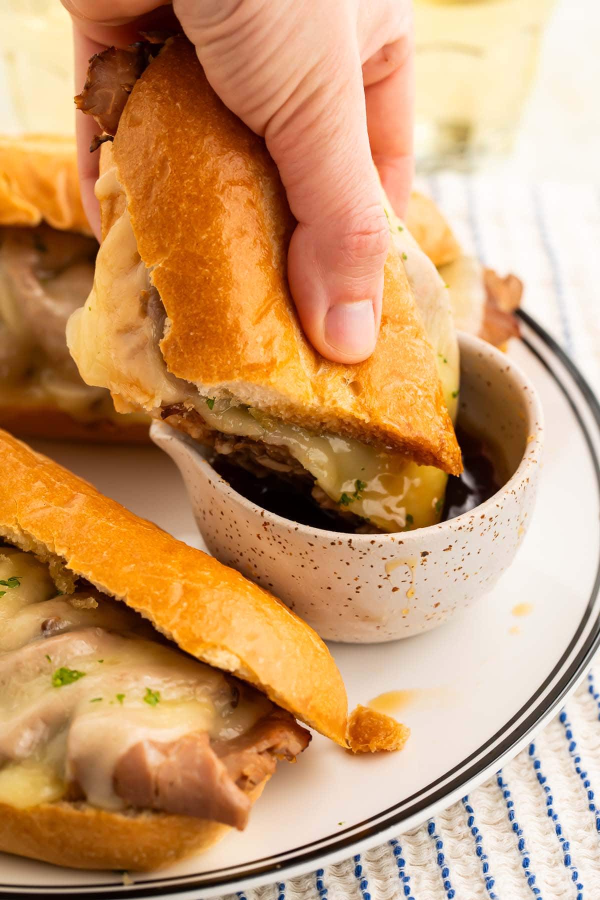 A french dip sandwich  served au jus being dipped into a small bowl of jus.