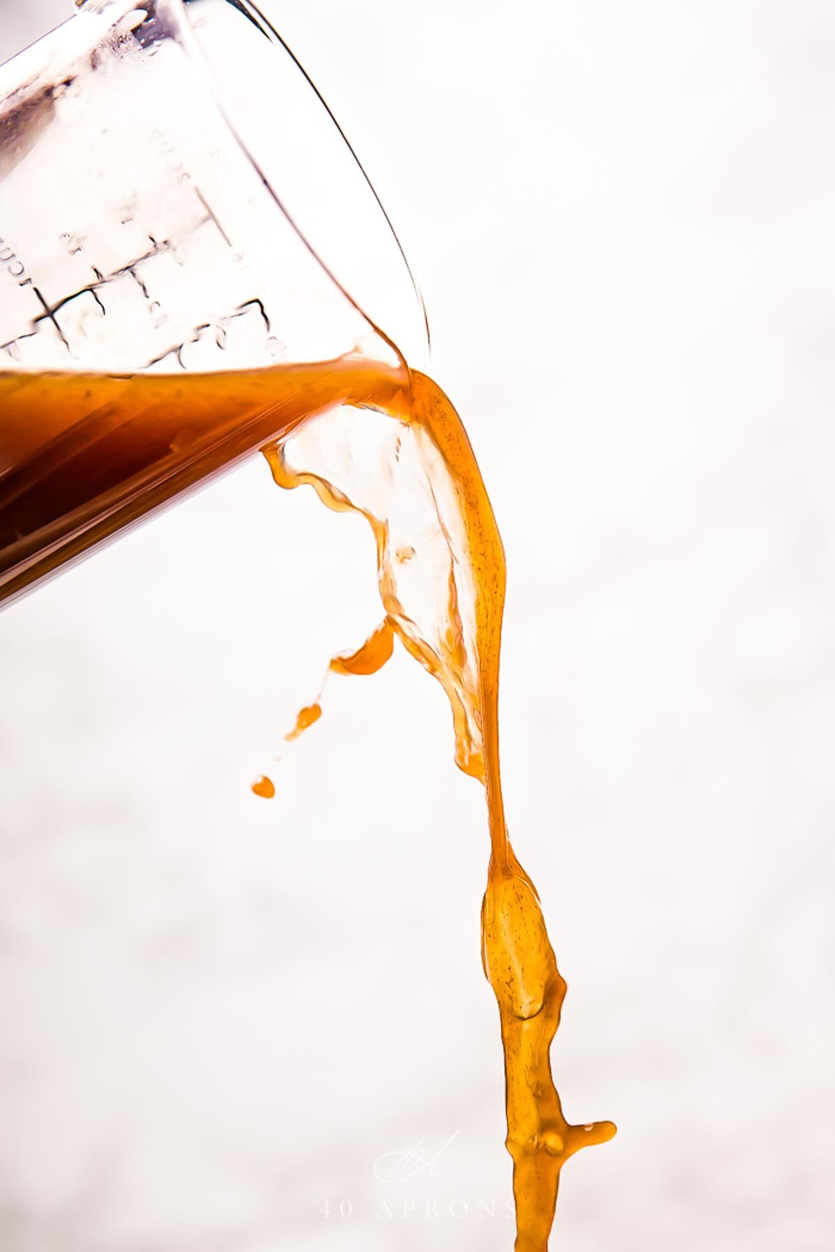 Rich au jus being poured out of a glass measuring cup in front of a white background.