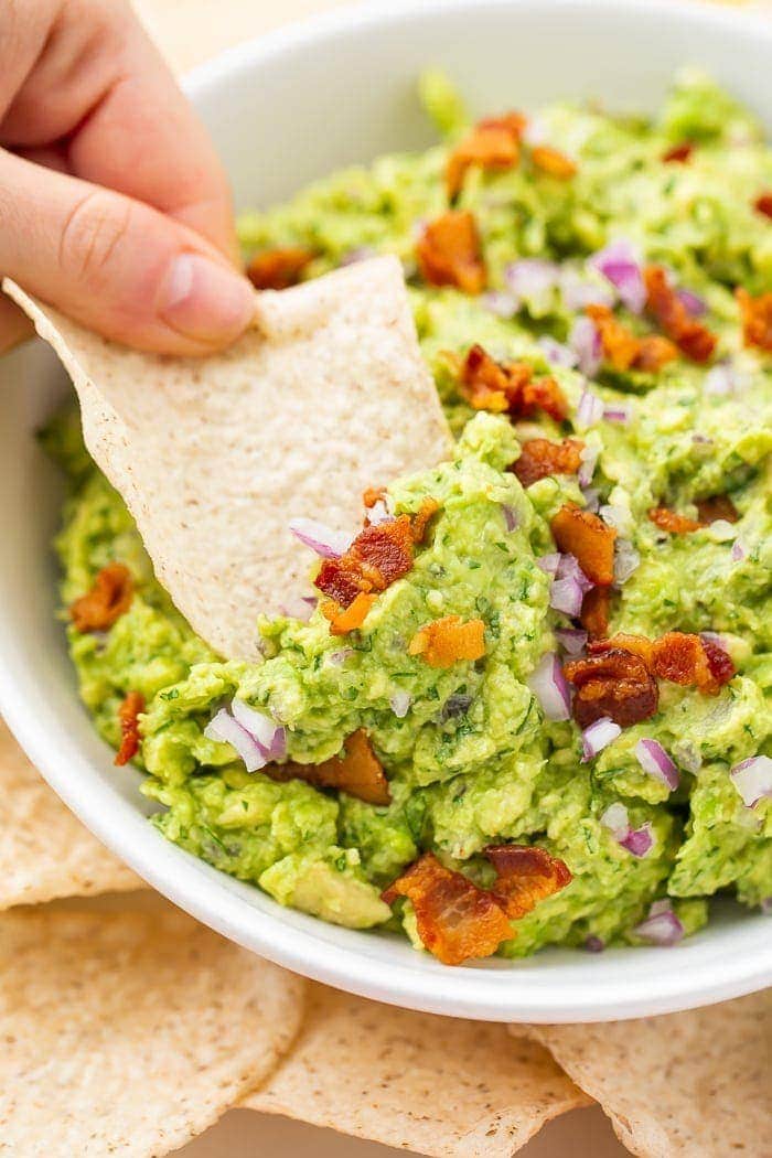 Bowl of bacon guacamole with a tortilla chip being dipped in