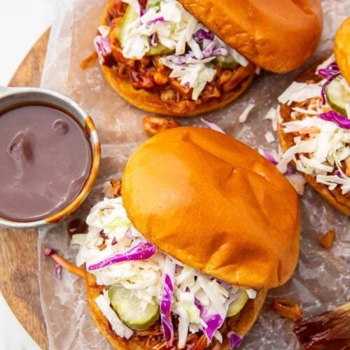 Three vegan BBQ jackfruit sandwiches with a side of barbecue sauce