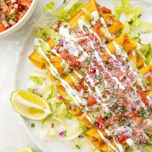 Plate of bean and cheese taquitos with limes and served with pico de gallo and avocado