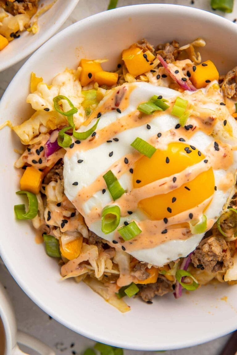 Breakfast sausage, mango, fried egg, coleslaw, and green onion in a white bowl