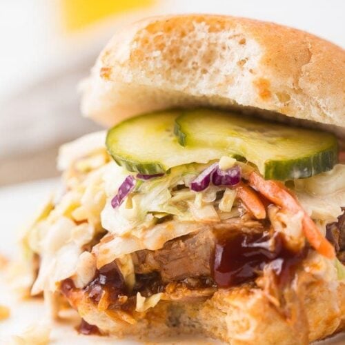 close up image of instant pot pulled pork served on hamburger bun with coleslaw, pickles, and barbecue sauce.