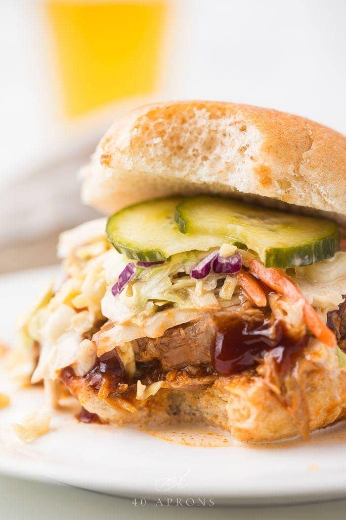 close up image of instant pot pulled pork served on hamburger bun with coleslaw, pickles, and barbecue sauce.