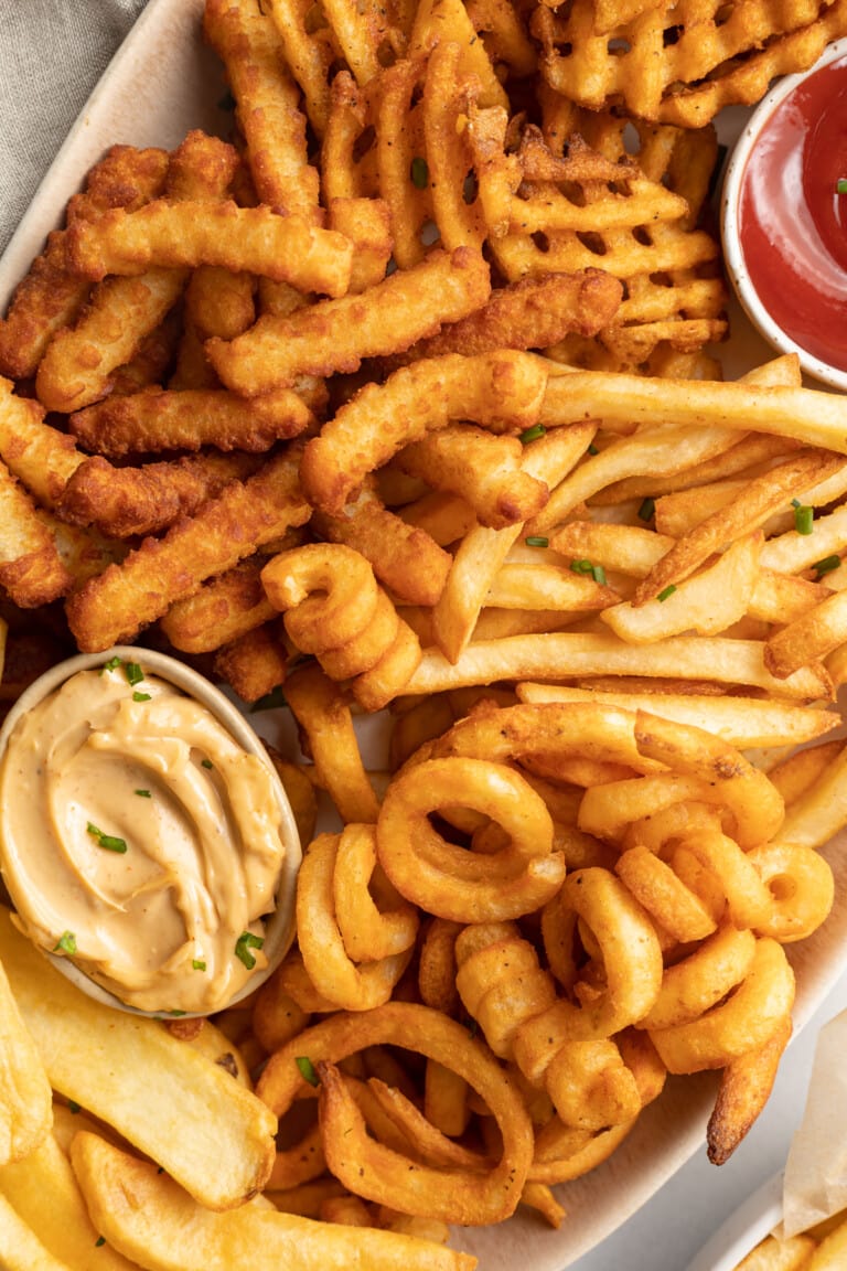 Overhead, closeup photo of various styles of frozen french fries on an oval shaped platter with a ramekin of ketchup