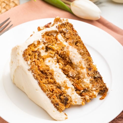 Slice of paleo carrot cake on a white plate resting on a light pink cloth napkin.