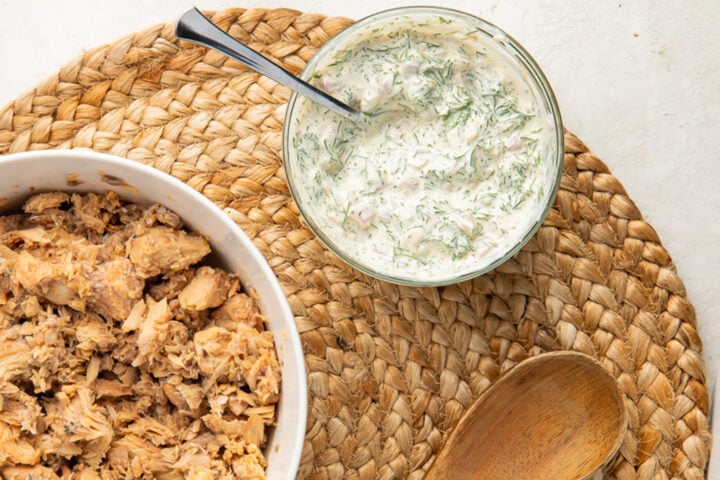 Creamy dill dressing in a small glass bowl next to a bowl of canned salmon.