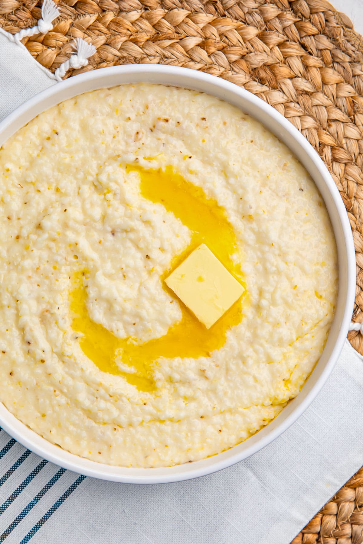 Overhead view of creamy grits in a white bowl, with a pat of melting butter swirled in the center of the bowl.