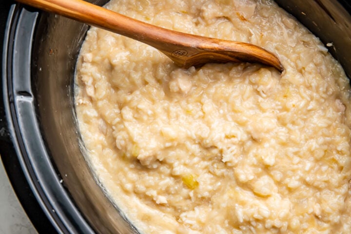 Creamy Crockpot chicken and rice in a black Crockpot insert with a wooden spoon.