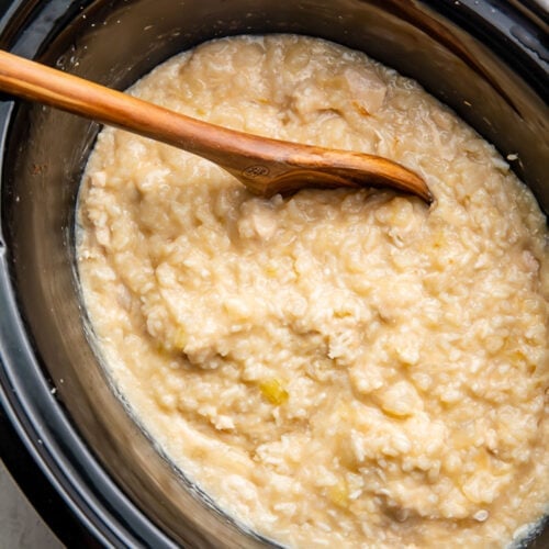 Creamy crockpot chicken and rice in a black Crockpot insert with a wooden spoon resting against the side.