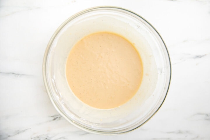 Buttermilk added to pancake batter ingredients in large glass mixing bowl.