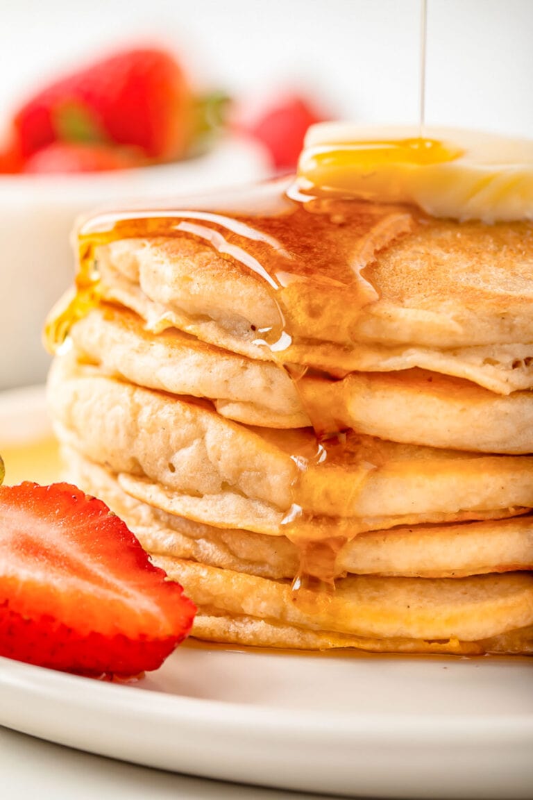 Syrup being poured over a stack of fluffy gluten-free pancakes topped with a pat of butter.