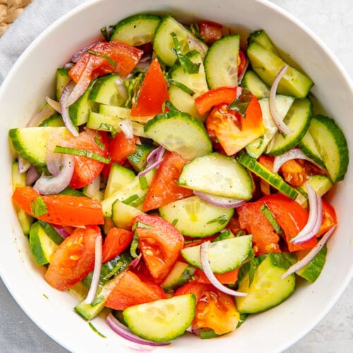 Top-down view of a large white bowl holding a fresh, vibrant cucumber tomato salad with slices of red onion.