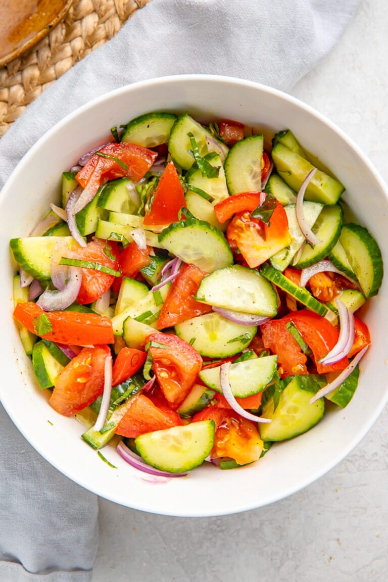 Top-down view of a large white bowl holding a fresh, vibrant cucumber tomato salad with slices of red onion.