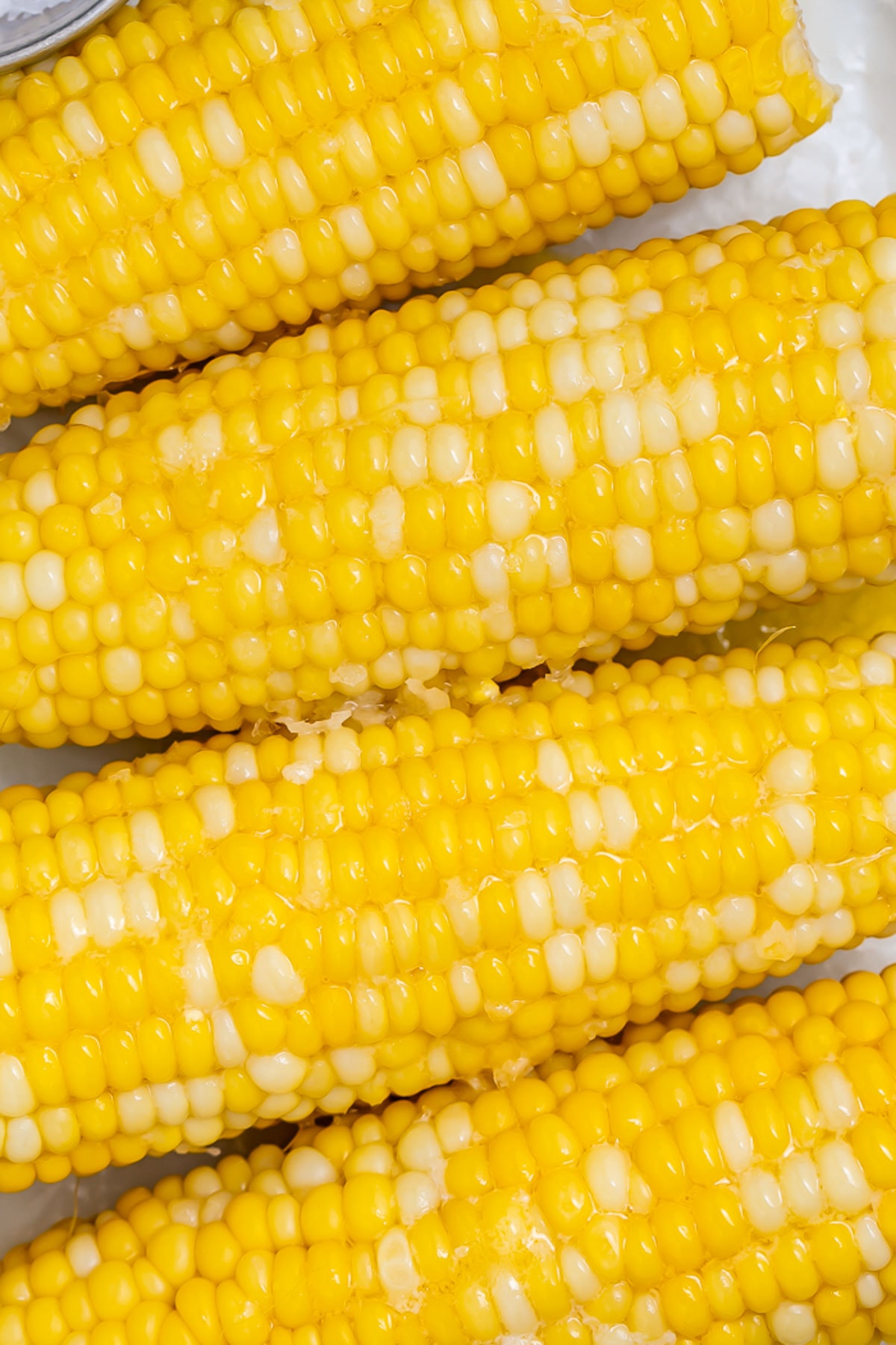 Close-up of 4 ears of boiled corn on the cob topped with melty butter.