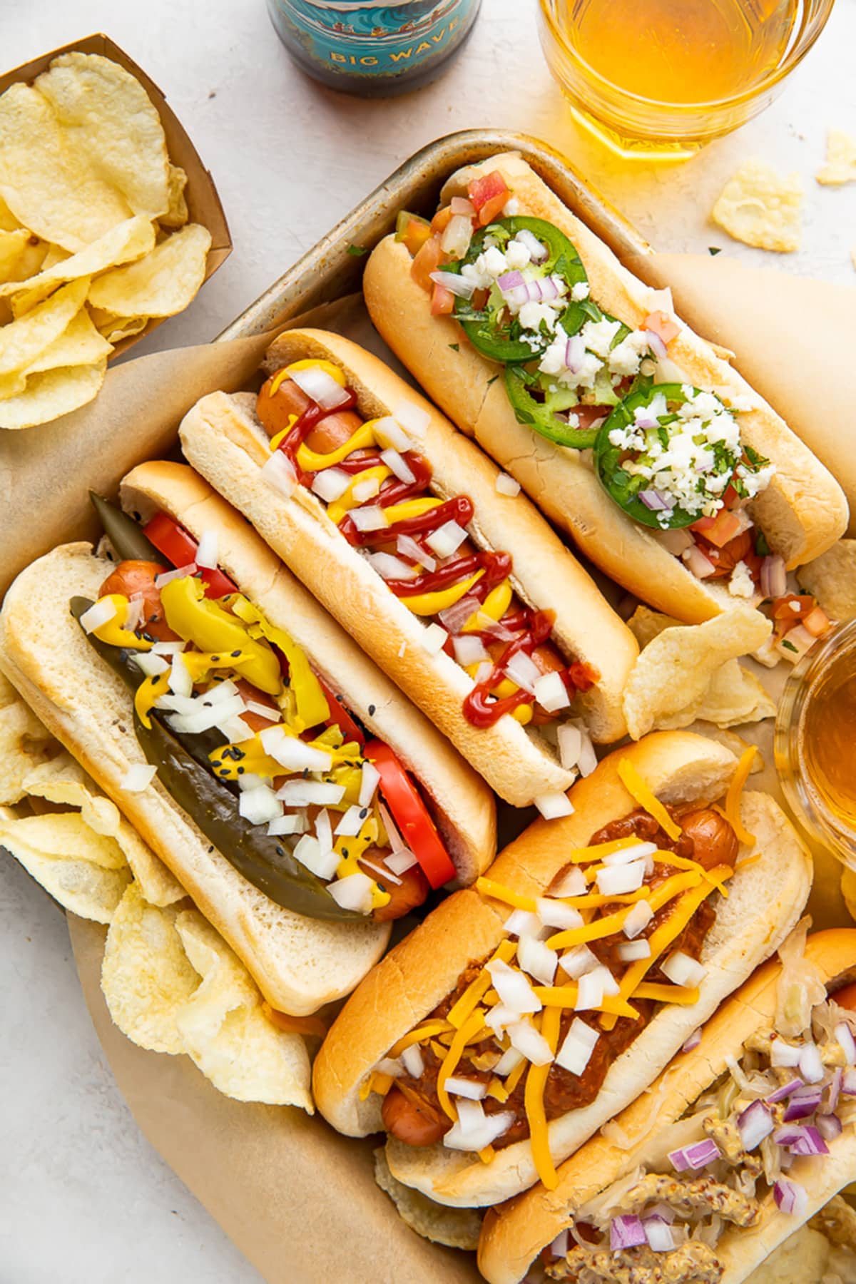 5 air fryer hot dogs in hot dog buns with various toppings arranged on a baking sheet.