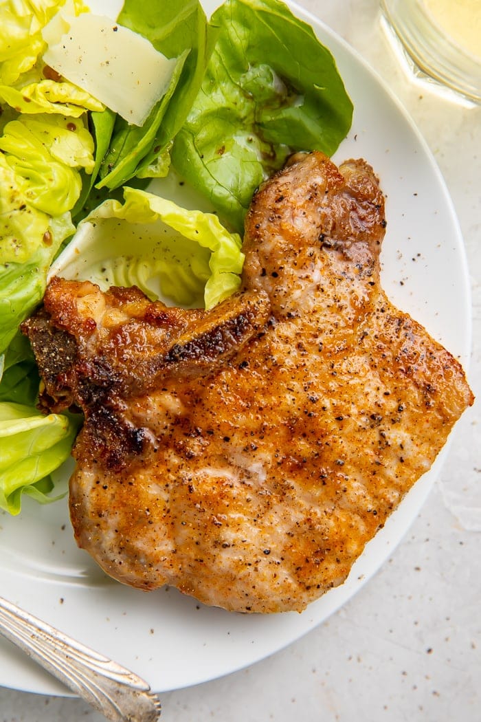 A pork chop on a plate next to some lettuce