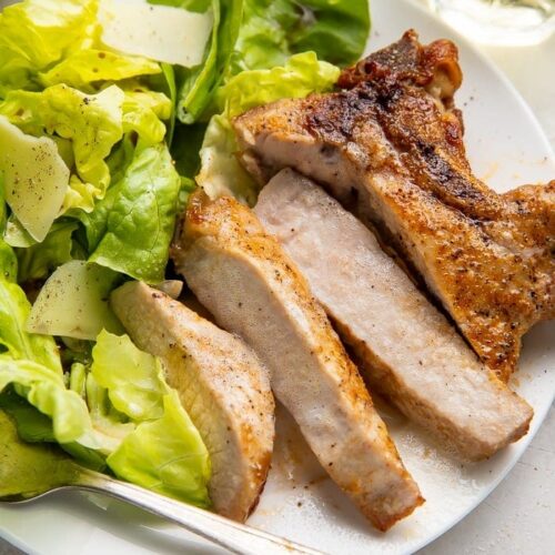 Sliced pork chop cooked in the air fryer with a bed of green veggies on a white plate