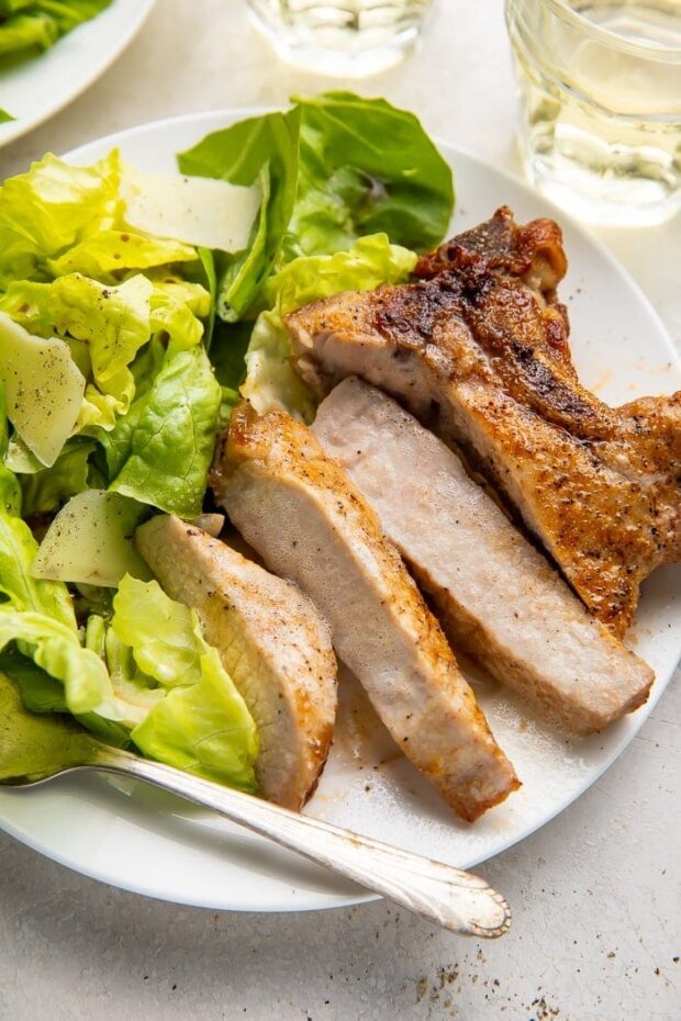 Sliced pork chop cooked in the air fryer with a bed of green veggies on a white plate