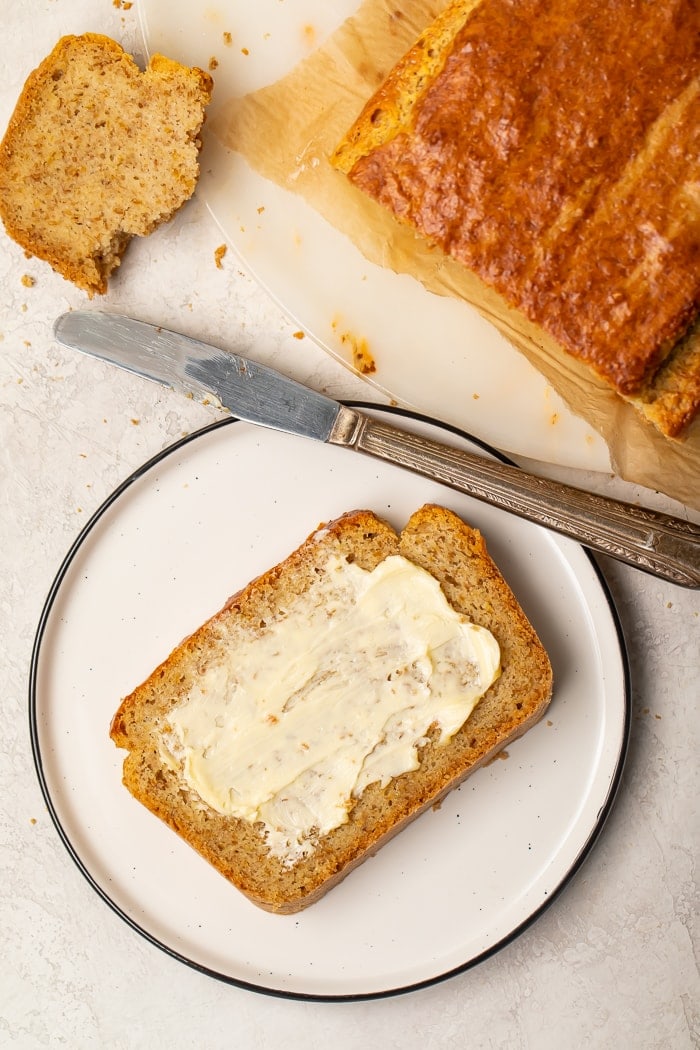 Slice of toasted paleo bread with butter on a white plate with a butter knife