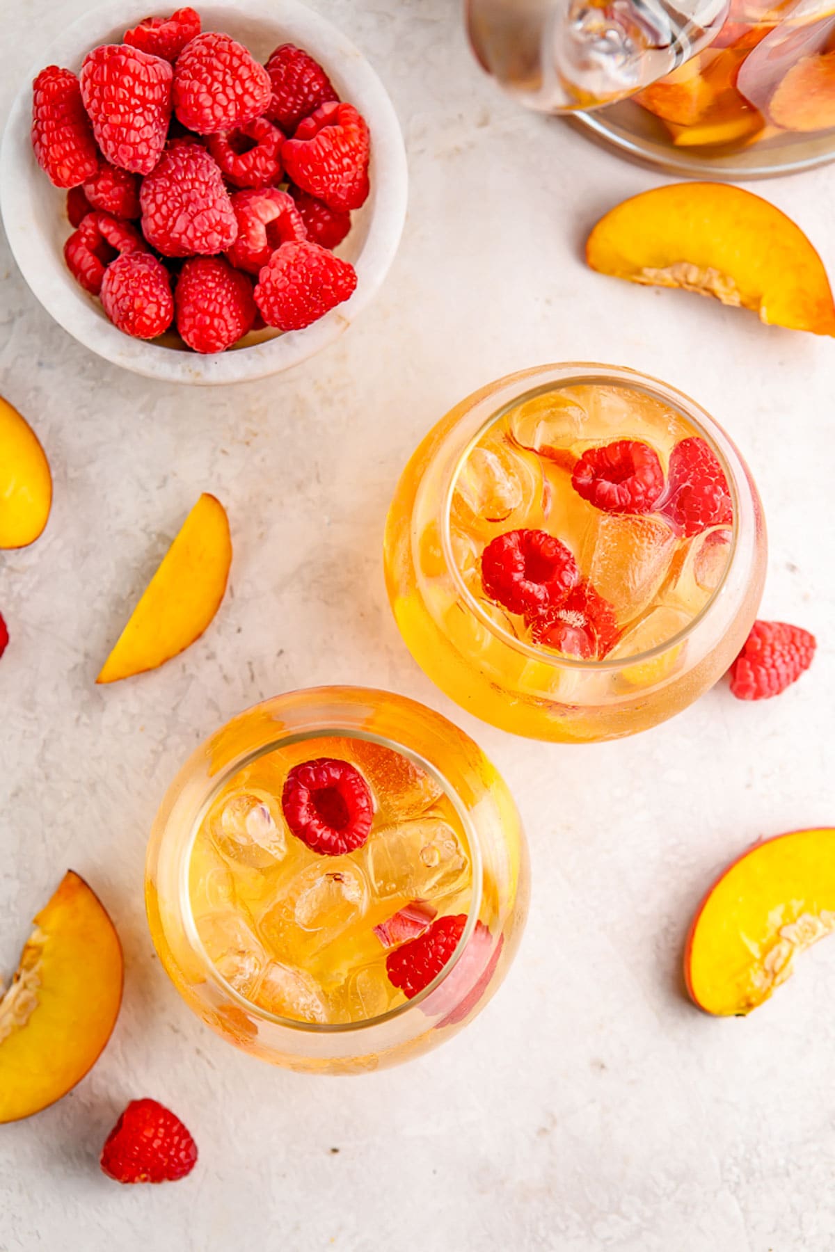 Overhead view of two stemless wine glasses holding peach white sangria garnished with fresh raspberries.