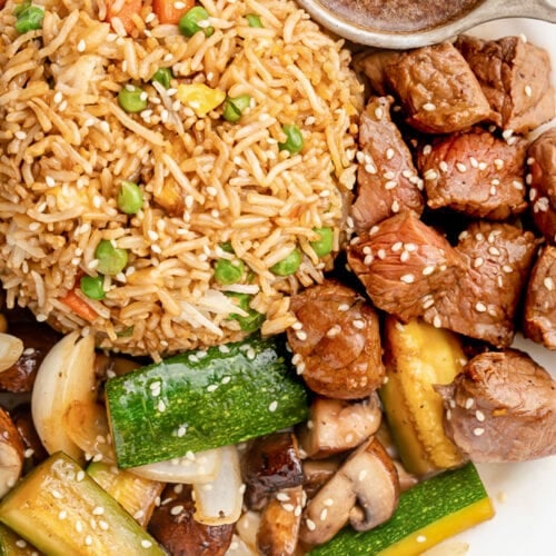 A close-up of hibachi steak garnished with sesame seeds on a plate with fried rice and stir-fry veggies.