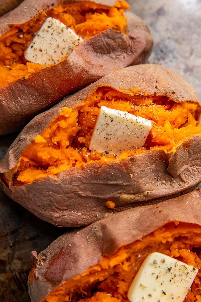 Close up of sweet potatoes cut open and stuffed with butter, salt, and pepper, on a white plate