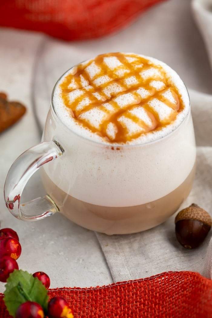 A glass mug of pumpkin caramel macchiato with lots of froth and a criss-cross design made of caramel sauce on the top