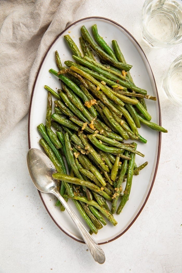 Overhead shot of an oval plate of green beans with a silver serving spoon