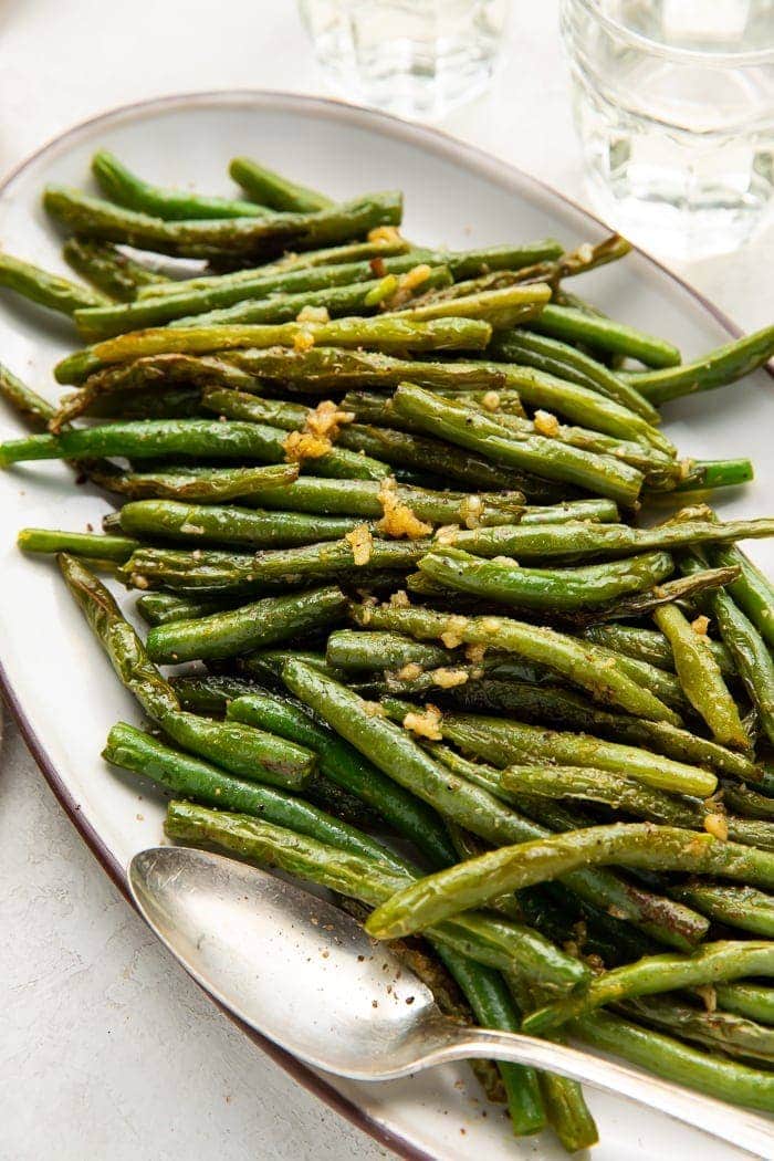 Overhead shot of a long oval plate of green beans with a silver serving spoon