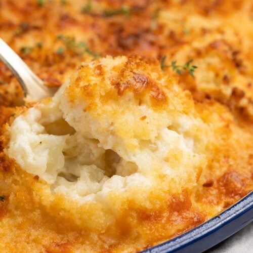 A spoonful of cauliflower au gratin being lifted from a baking dish