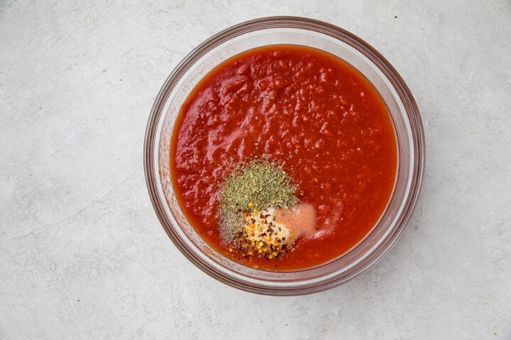 Crushed tomatoes and spices for homemade marinara in a large glass bowl.