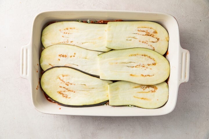 Second layer of 6 thinly-sliced eggplant slices on top of ricotta and marinara in a casserole dish.