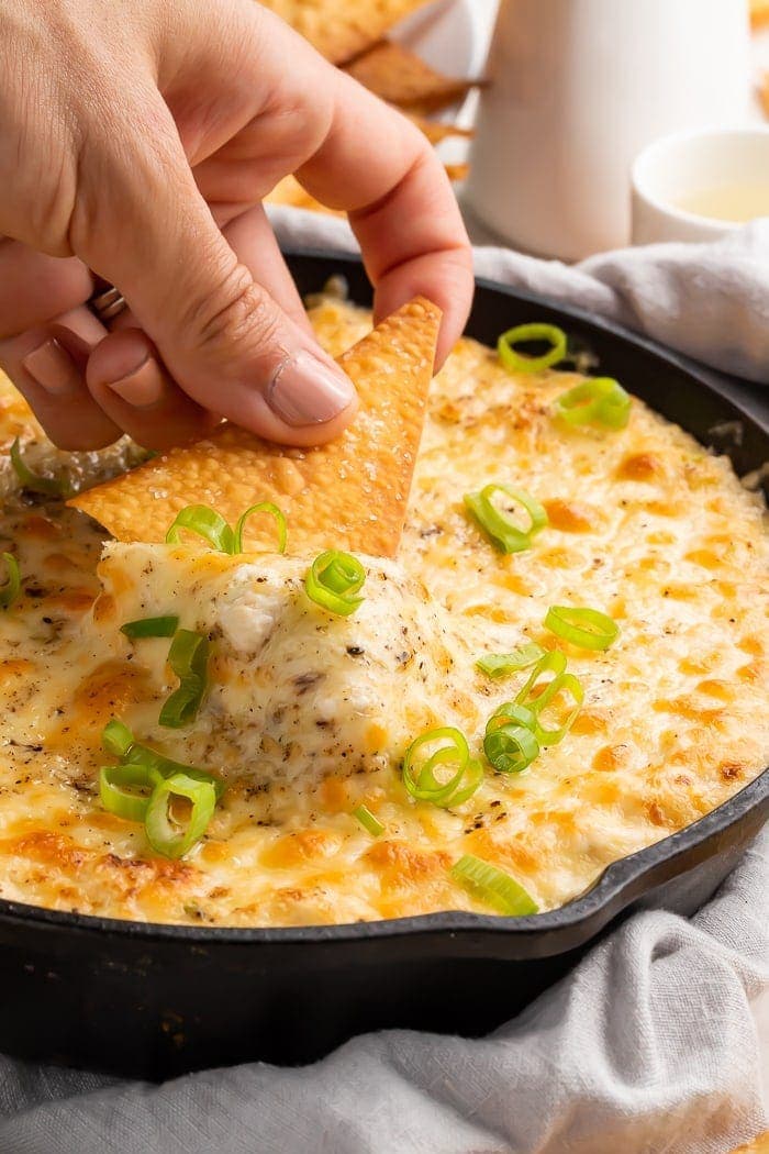 A hand dipping a chip into a cast iron skillet of crab rangoon dip