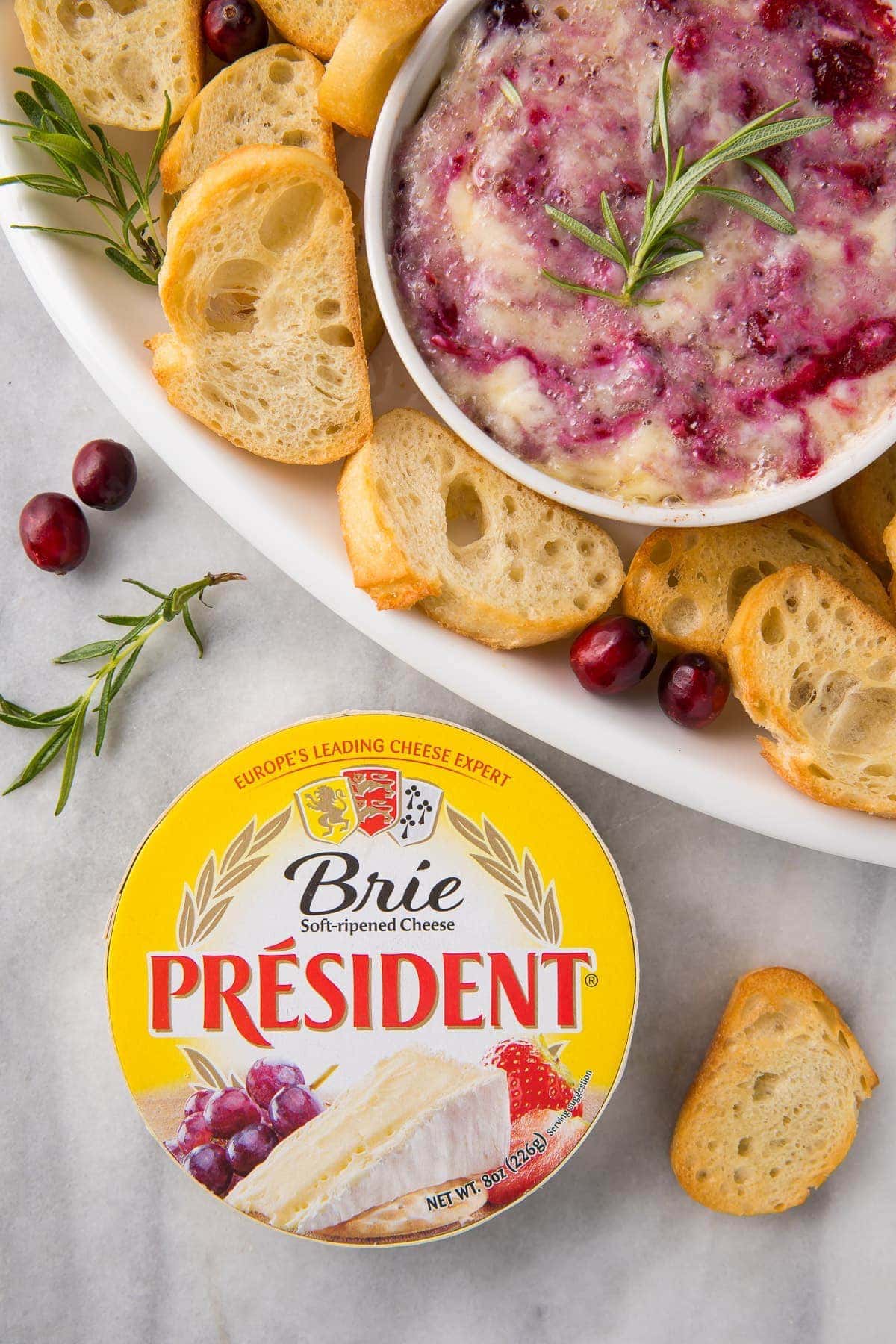 A serving tray with crackers and cranberry brie dip with a package of President Brie