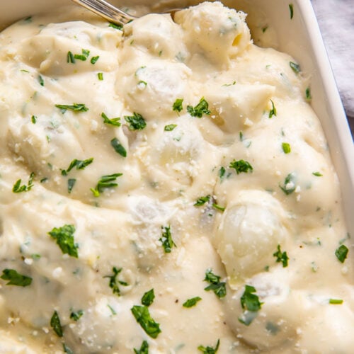 Creamed onions garnished with fresh herbs in a casserole dish.