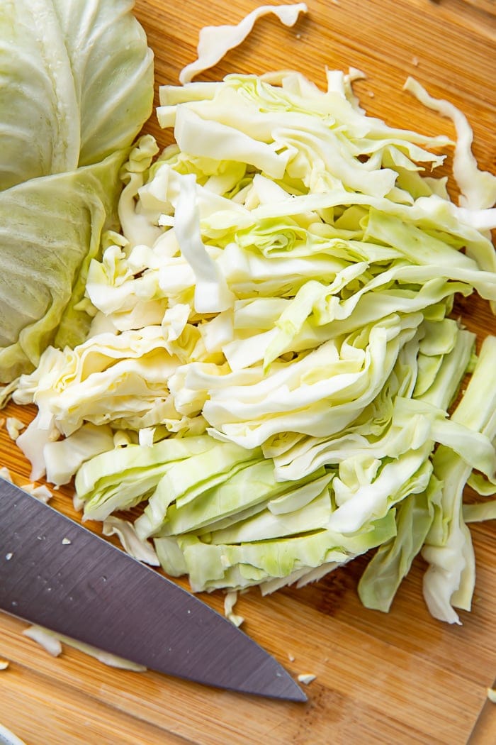 Shredded cabbage on a wooden cutting board next to a knife