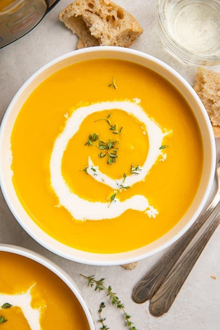 A bowl of butternut squash soup with a drizzle of cream inside a white bowl