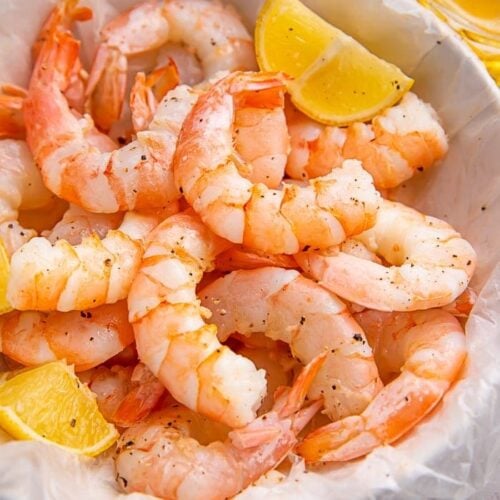 Instant Pot shrimp in a white bowl with lemon wedges