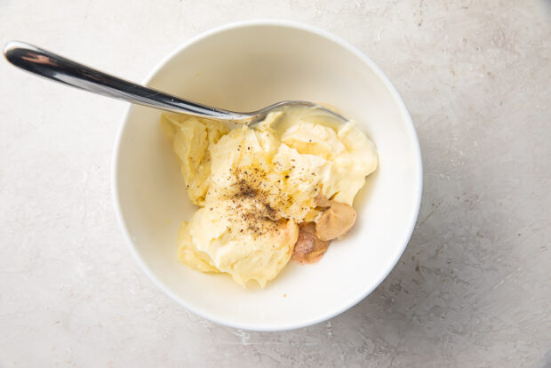 Mayonnaise, garlic, lemon juice, and salt in a white mixing bowl before becoming garlic aioli